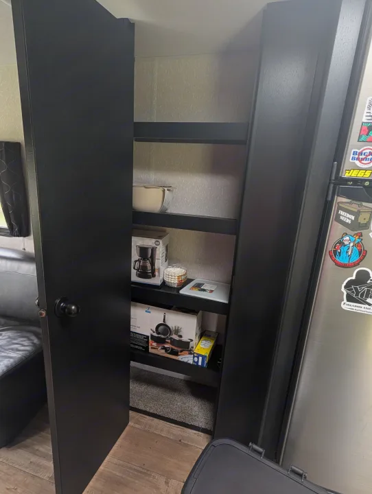 RV rental: Interior view of kitchen pantry storage with shelves, a coffee maker, cookware, and a sticker-decorated fridge.. Forest River Cherokee Grey Wolf 2021