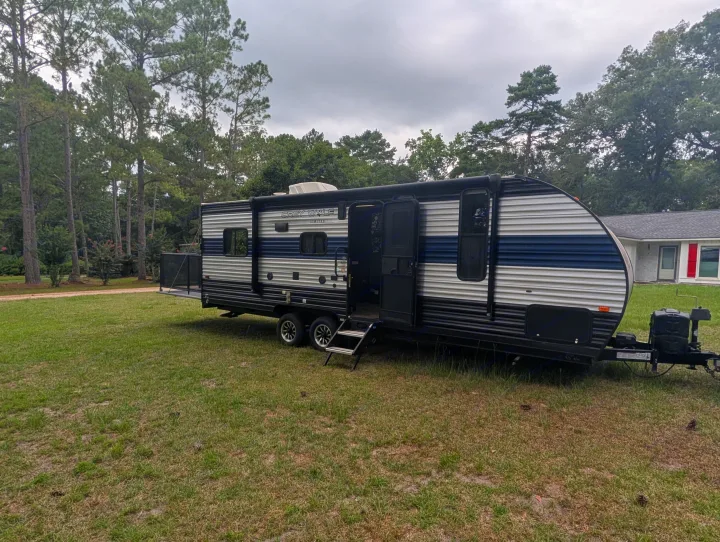 This Grey Wolf RV rental, with its door open and steps down, is parked on grass, ready for a camping adventure.. Forest River Cherokee Grey Wolf 2021