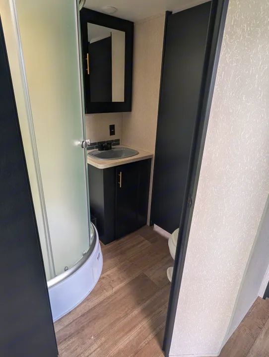 Compact RV rental bathroom with a frosted glass shower, black vanity, sink, and partially visible toilet. Features a modern, functional design.. Forest River Cherokee Grey Wolf 2021