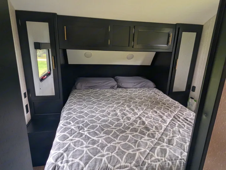 Experience compact comfort in this RV rental's bedroom, featuring dark cabinets, a patterned bed, and essential amenities.. Forest River Cherokee Grey Wolf 2021