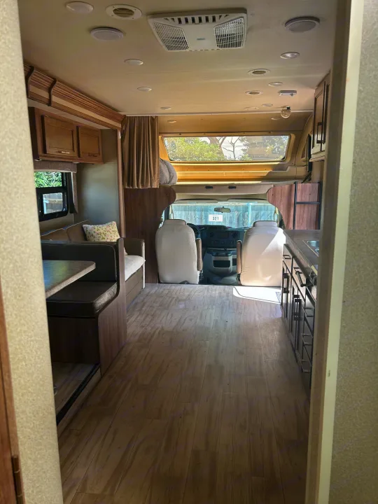 Inside an rv rental, revealing its dinette, kitchen area, driver's cab, and overhead bunk.. Entegra Coach Odyssey 2019