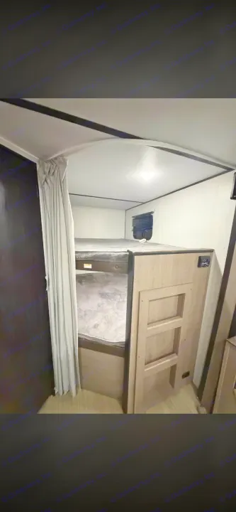 Cozy RV rental bunk beds with a ladder, privacy curtain, window, and overhead light for comfortable travel.. Keystone RV Hideout LHS 2020