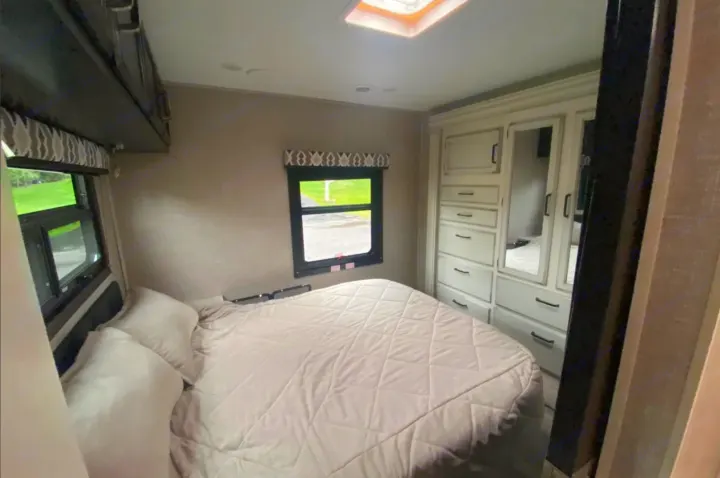 Cozy RV rental bedroom with a large bed, windows, overhead cabinets, and built-in dresser.. Jayco Redhawk 2022