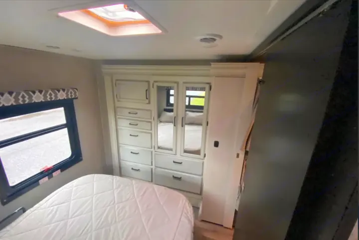 Cozy RV rental bedroom featuring a white bed, window, and mirrored dresser/wardrobe. Perfect for comfortable travel.. Jayco Redhawk 2022