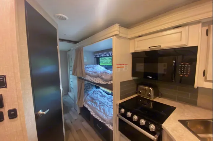 Inside this RV rental, view stacked bunk beds, plus a compact kitchen with microwave, toaster, stove, and sink.. Jayco Redhawk 2022