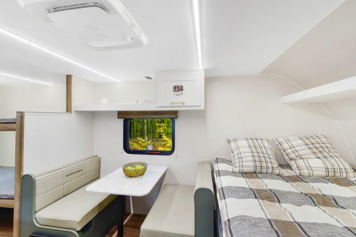 Modern rv rental interior with bright white walls, a comfy dinette, bunk beds, and a sleeping area overlooking a forest.. Heartland RVs Eddie Bauer 2025