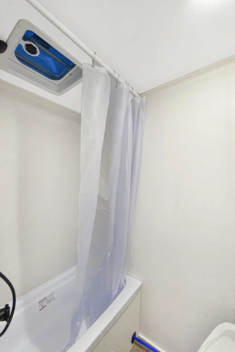 This compact RV rental bathroom features a tub, shower curtain, and overhead vent for comfortable travel.. Heartland RVs Eddie Bauer 2025