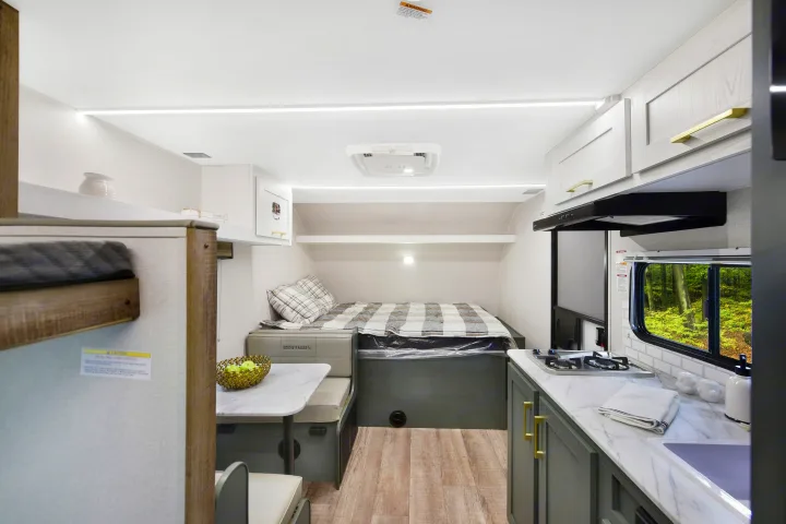 Modern RV rental interior features a cozy bed, dinette, and fully equipped kitchen with a forest view.. Heartland RVs Eddie Bauer 2025