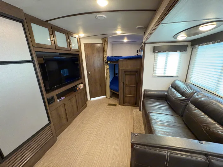 Modern RV rental interior with a living area, dark leather sofa, entertainment center, refrigerator, and bunk beds.. Keystone RV Passport Grand Touring 2020
