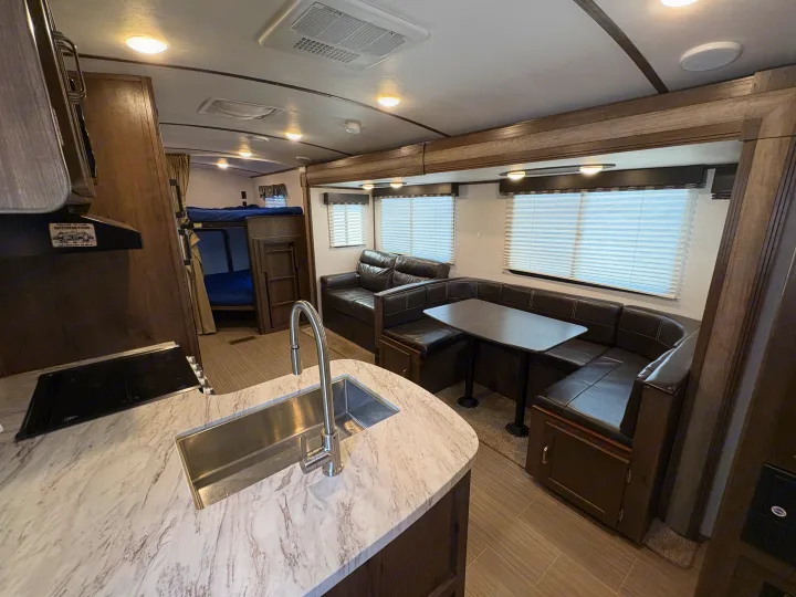 Explore this clean rv rental interior featuring a modern kitchen with a sink, bunk beds, and a comfy dinette & sofa.. Keystone RV Passport Grand Touring 2020