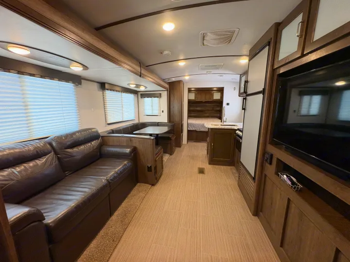 Spacious rv rental interior featuring a brown leather sofa, dinette, kitchen, and bedroom. Modern wood and light finishes.. Keystone RV Passport Grand Touring 2020