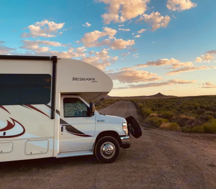 A white Redhawk rv rental, an E450 motorhome, parked on a remote dirt road in a vast, brushy landscape under a cloud-streaked sky.. Jayco Redhawk 2016