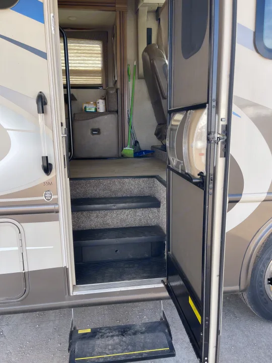 RV rental motorhome entrance: Open main and screen doors show interior steps leading to the living area, with cleaning supplies.. Thor Windsport 2019