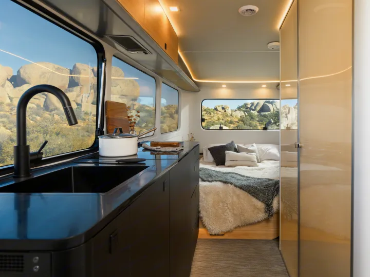 This sleek RV rental features a modern kitchen with a black sink, leading to a cozy bedroom. Large windows showcase a stunning desert view.. Pebble Flow 2026