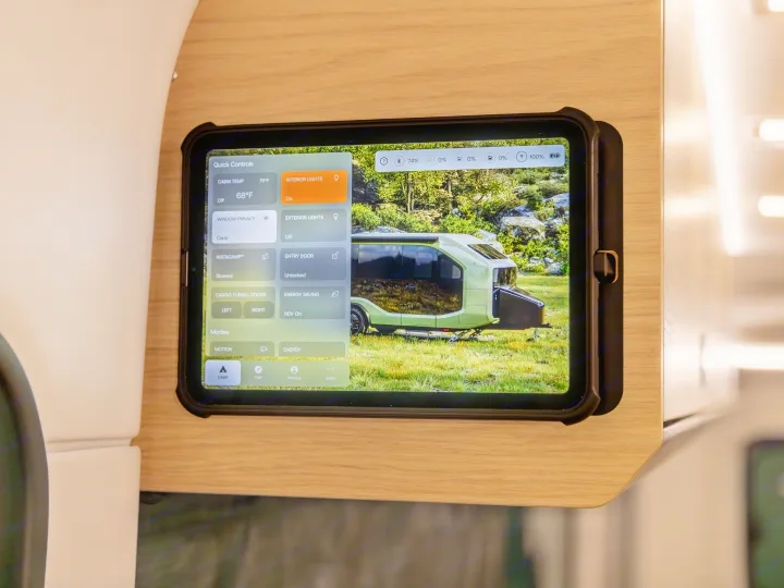 An rv rental's smart tablet interface displays Quick Controls for cabin temp, lights, and door lock, with a camper background.. Pebble Flow 2026