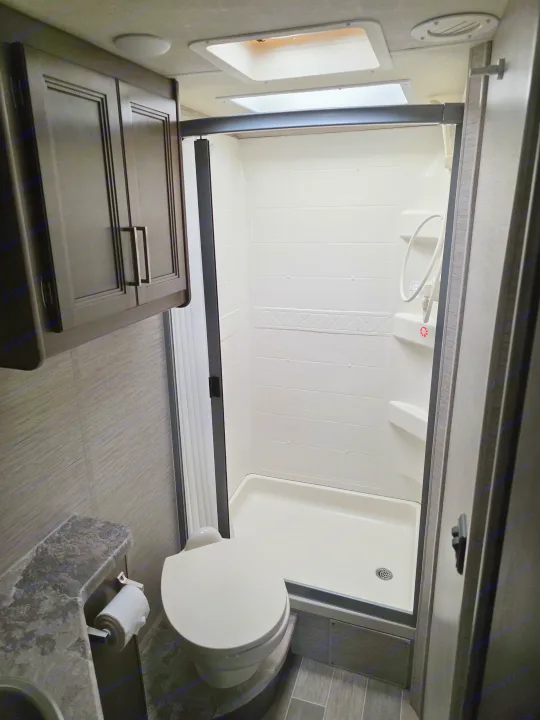 Clean rv rental bathroom featuring a stand-up shower, toilet, vanity, and overhead cabinets for comfortable travel.. Thor Chateau 2021