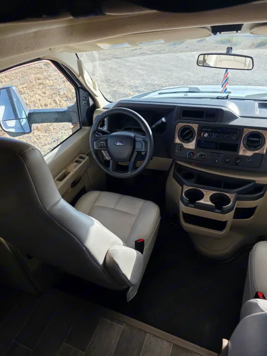 RV rental interior: spacious front cab with Ford steering wheel, light beige seats, dashboard, and large side mirrors.. Thor Chateau 2021