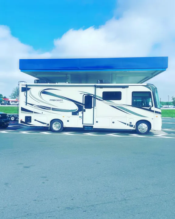 White Precept Jayco motorhome, perfect for an rv rental adventure, parked at a gas station with a towed car. Blue sky above.. Jayco Precept 2022