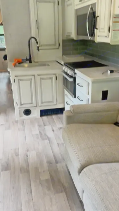 Modern RV rental kitchen and living area, featuring white cabinets, gray backsplash, wood-look flooring, and a sofa.. Jayco Precept 2022