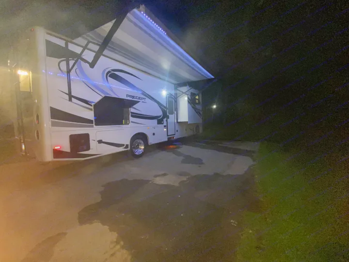 Brightly lit rv rental motorhome at night, featuring an extended awning with blue LEDs and an outdoor kitchen.. Jayco Precept 2022