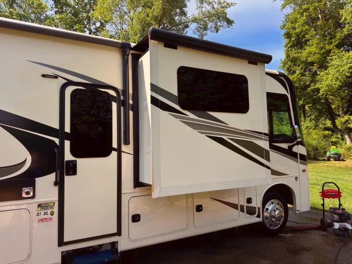 Cream RV rental with extended slide-out, parked near trees, with a pressure washer visible, ready for cleaning.. Jayco Precept 2022
