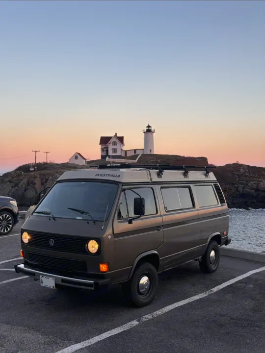 A classic brown VW Westfalia camper, perfect for RV rental trips, by a Maine lighthouse at golden hour.. Volkswagen Westfalia 1985