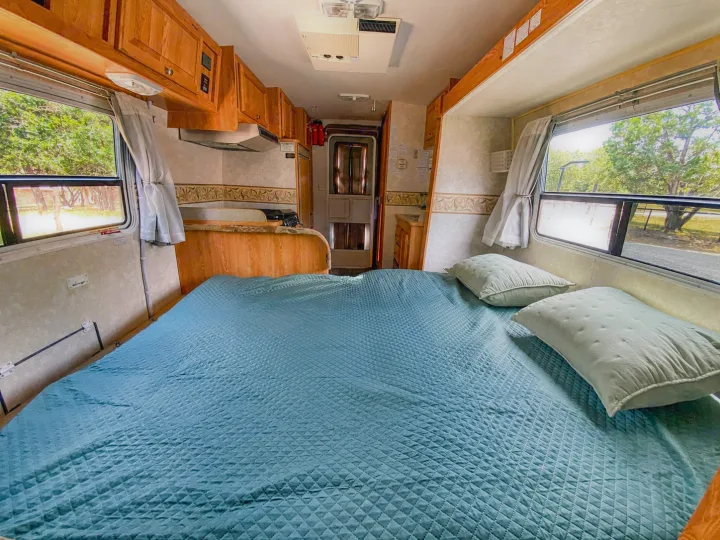 Cozy RV rental interior showcasing a spacious bed, functional kitchen, and scenic window views for camping.. R-Vision Trail-Lite 2002