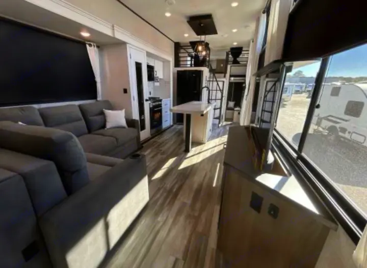 This modern rv rental interior features a large gray sectional, full kitchen, and unique loft beds. Bright and ready for trips!. Jayco Jay Flight Bungalow 2025
