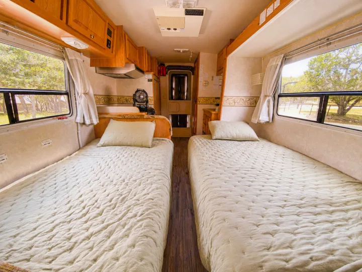 Cozy twin beds in an RV rental, with light quilted bedding, windows, and wooden cabinetry for travelers.. R-Vision Trail-Lite 2002