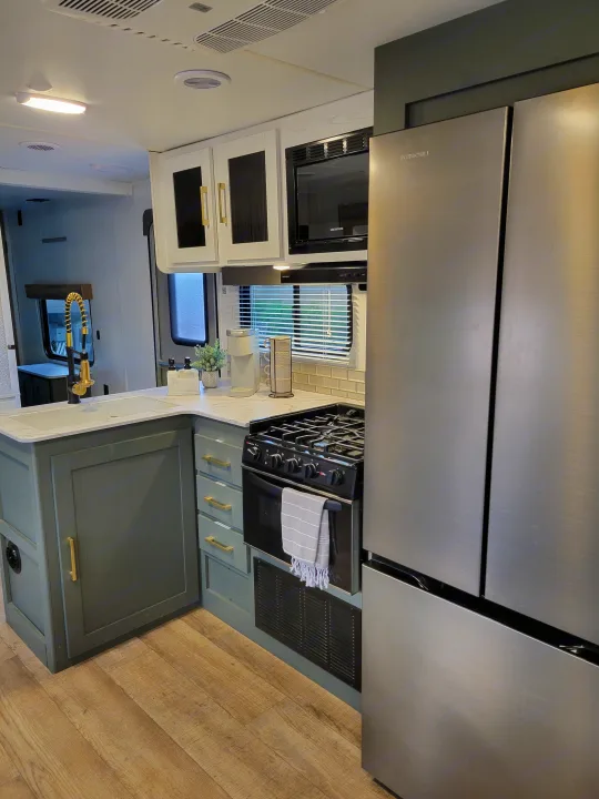 Spacious RV rental kitchen featuring modern green cabinets, stainless steel appliances, white counters, and wood flooring.. Heartland RVs Eddie Bauer 2024