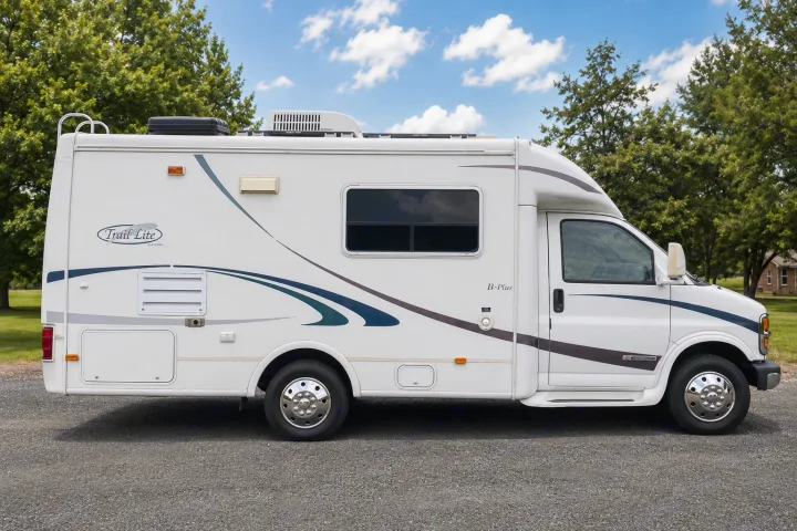 Side view of a white Trail Lite B-Plus RV rental motorhome, parked on gravel. Features windows, AC unit, and graphics.. R-Vision Trail-Lite 2002