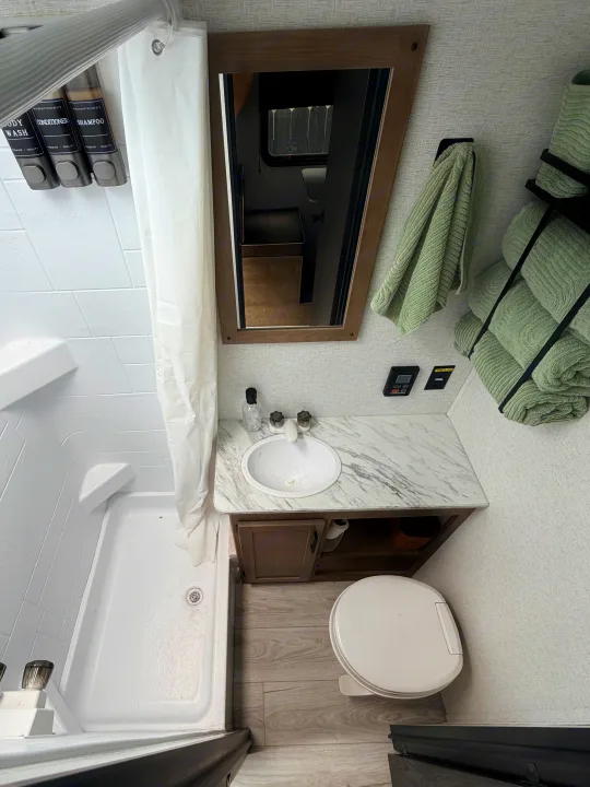 This clean, modern rv rental bathroom features a shower, toilet, vanity with sink, and wall-mounted amenity dispensers.. Keystone RV Springdale Mini 2025