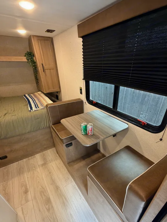 This RV rental interior features a cozy bed, dinette with drinks, and window for private views.. Keystone RV Springdale Mini 2025