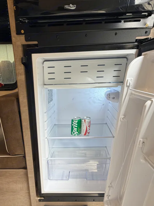 An open mini-fridge in an RV rental, containing Sprite and Diet Coke cans. A High Pointe microwave is above.. Keystone RV Springdale Mini 2025