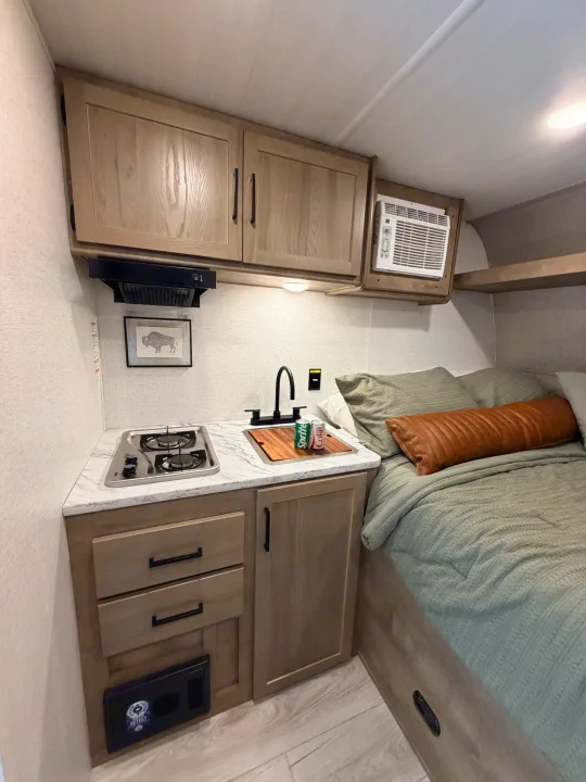 Compact RV rental interior: functional kitchenette with stove & sink, plus a comfy bed. Ready for your adventure.. Keystone RV Springdale Mini 2025