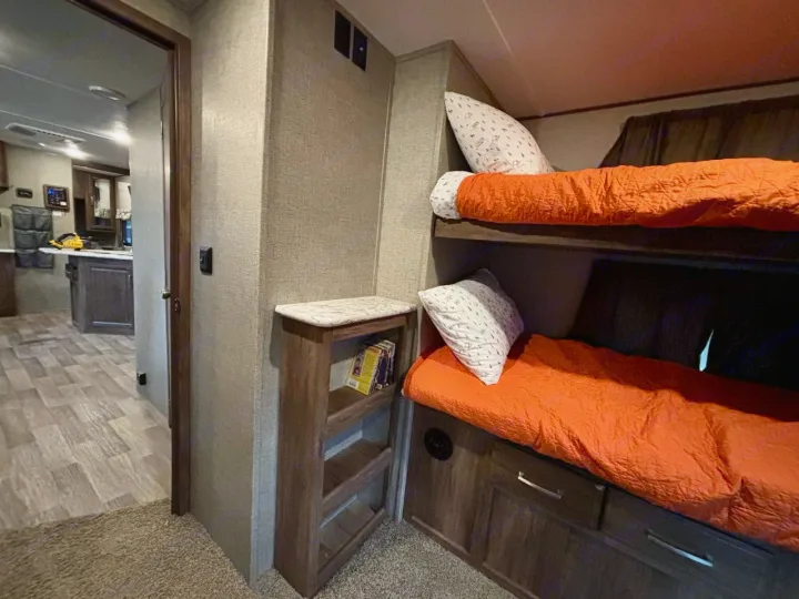 Cozy RV rental bunk beds with orange bedding and storage, looking into the kitchen/living area with wood floors.. Keystone RV Cougar 2018