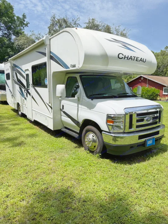 A clean white Thor Chateau Class C RV rental with graphics, parked on a sunny green lawn, ready for travel.. Thor Chateau 2025