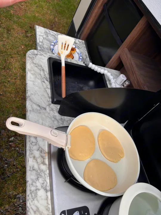 Fresh pancake batter in a pan on an RV rental's outdoor stove. A spatula sits near the sink with cooked pancakes ready.. Keystone RV Cougar 2018