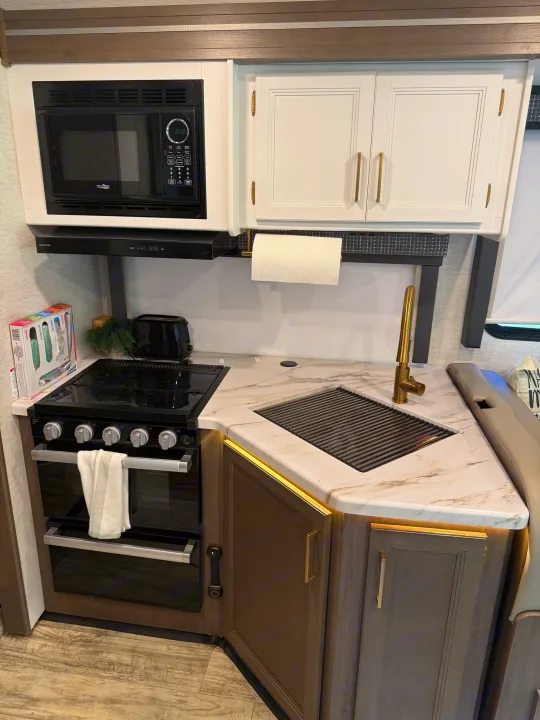 Explore this RV rental's modern kitchen with a black microwave, stove, gold faucet, and marble-look counters for stylish travel cooking.. Thor Chateau 2025