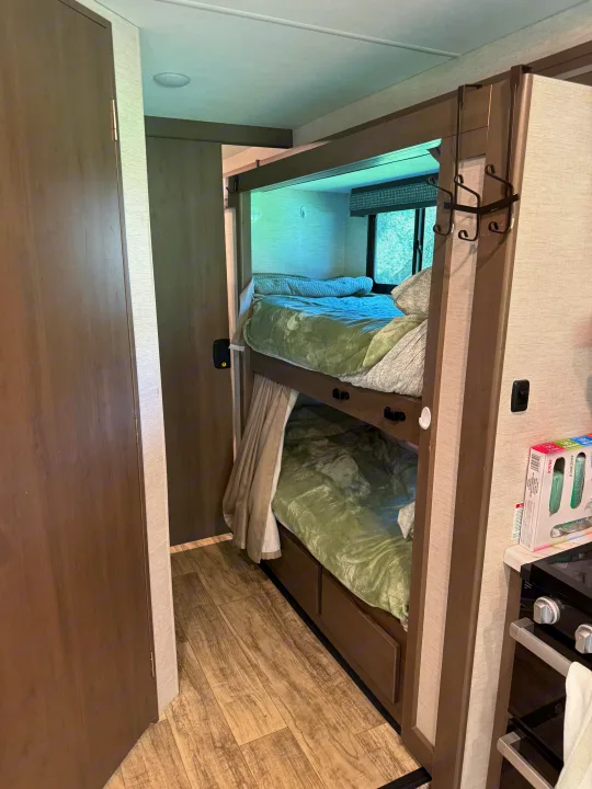 RV rental: Compact bunk beds with light green bedding, a window, an adjacent door, and a glimpse of the kitchen area.. Thor Chateau 2025