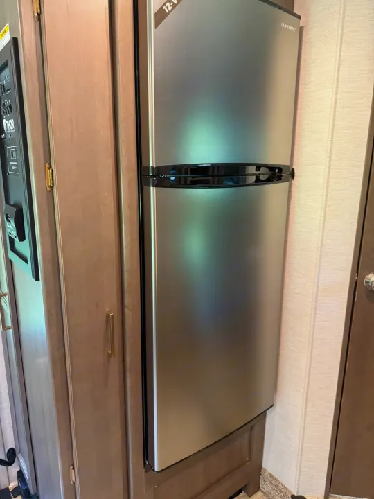 RV rental interior: modern 12-V stainless steel refrigerator, Thor control panel, and wood cabinetry.. Thor Chateau 2025