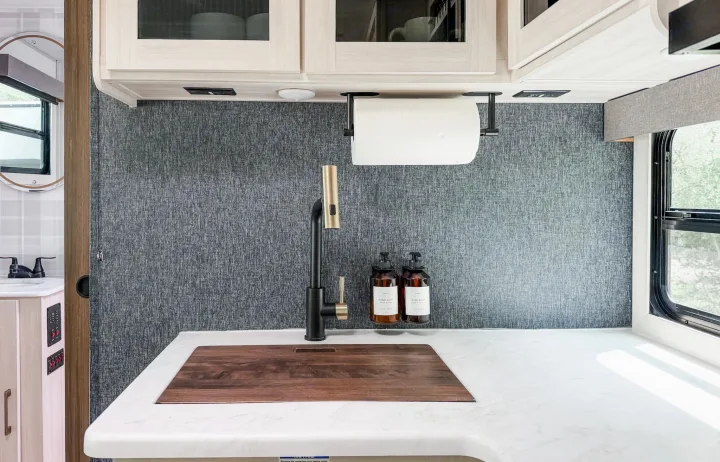 Modern RV rental kitchen: black & gold faucet, white counters, textured gray walls. A clean, stylish interior.. Forest River Surveyor Legend 2026