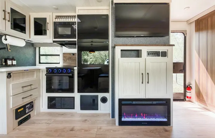 Modern RV rental interior: kitchen with oven, microwave, fridge, cozy fireplace, entertainment, and dining space.. Forest River Surveyor Legend 2026