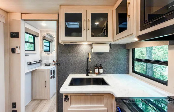 Modern RV rental interior featuring a stylish kitchen with sink, light wood cabinets, and an adjacent bathroom.. Forest River Surveyor Legend 2026