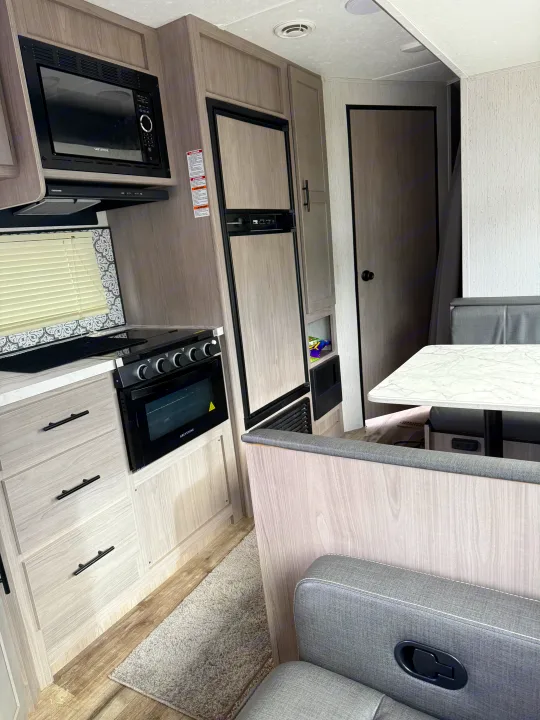 Modern rv rental interior featuring a light wood kitchen with microwave, stove, fridge, and a gray dinette area.. Coleman Lantern 2022