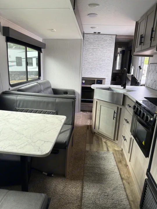Modern RV rental interior, featuring a gray dinette, marbled table, and full kitchen with sink, oven, and light wood cabinetry.. Coleman Lantern 2022