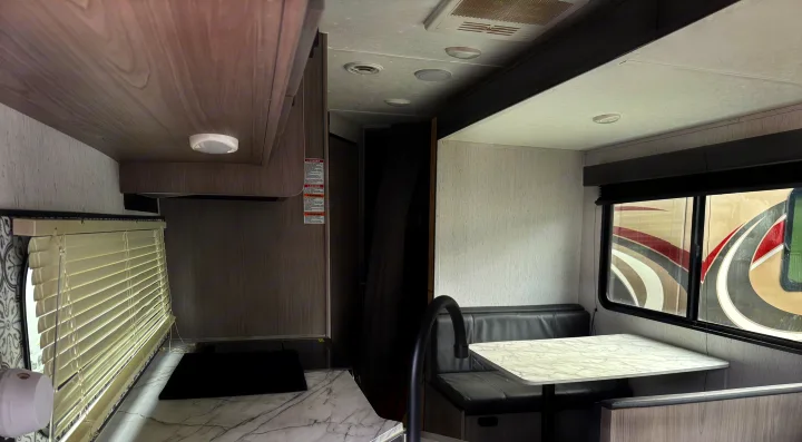 RV rental interior. Modern kitchen with white counters, sleek faucet, & dining booth. Light wood-grain walls, bright, airy space.. Coleman Lantern 2022