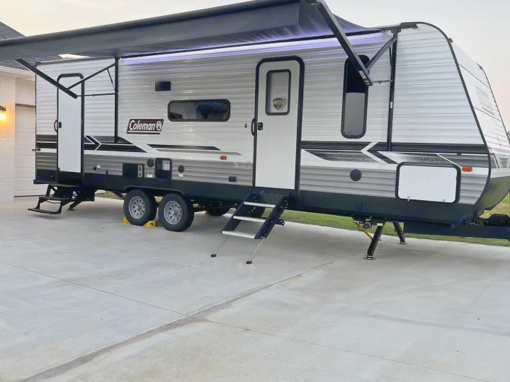 Modern Coleman travel trailer RV rental with illuminated awning and steps, set up on concrete, ready for your road trip.. Coleman Lantern 2022