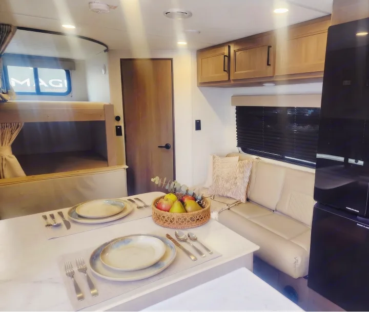 Modern RV rental interior: cozy dining area with a fruit basket, comfortable bunk beds, and a cream-colored sofa.. Grand Design Transcend Xplor 2025