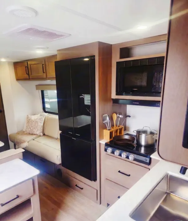 Modern RV rental kitchen with stove, microwave, fridge, and cozy seating. Perfect for your next travel adventure.. Grand Design Transcend Xplor 2025